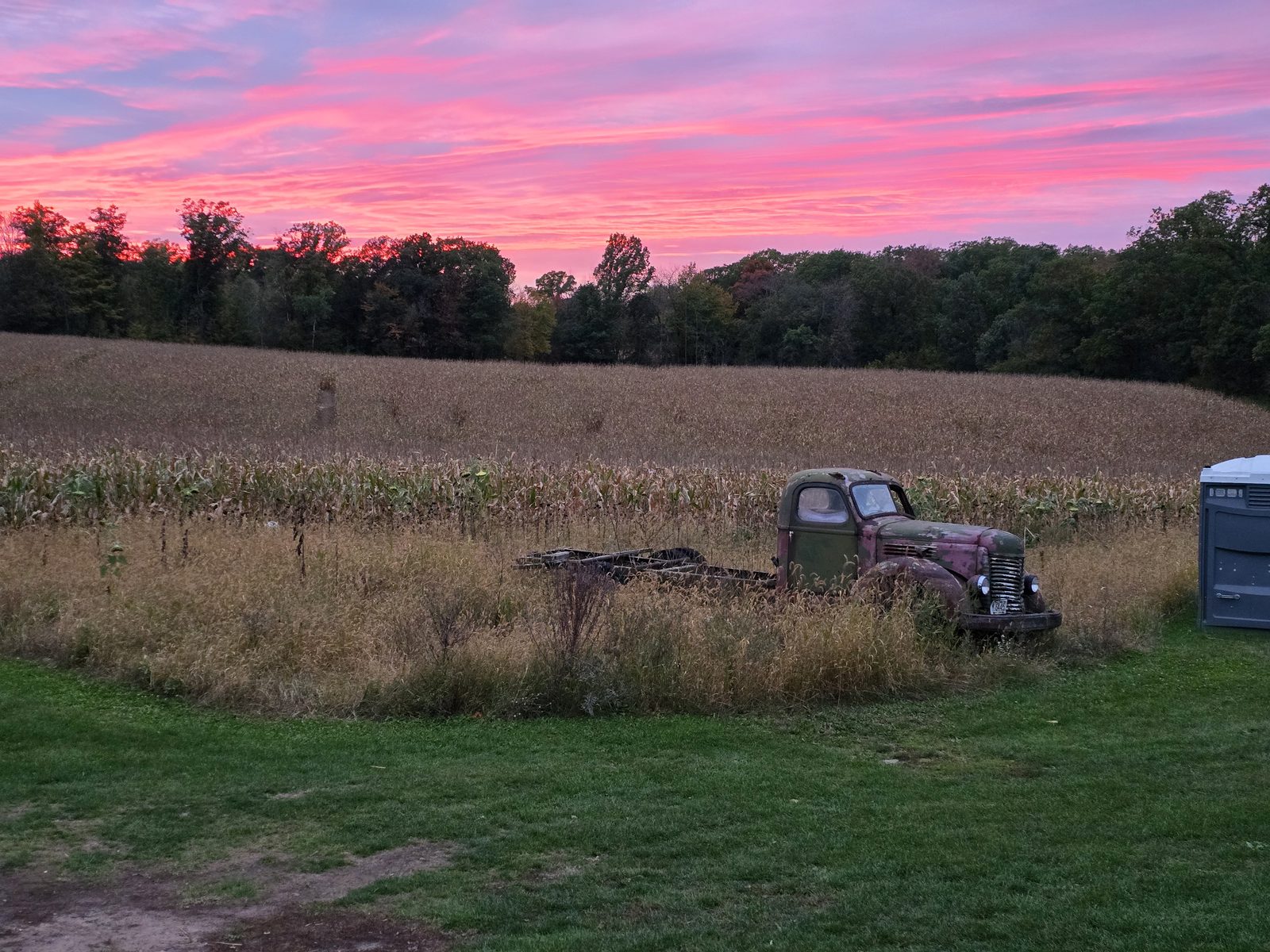 Old truck in a farm field under a pink October sunset sky