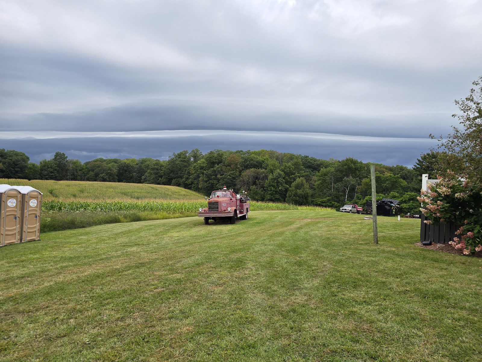 Farm lawn and cornfield under a long band of autumn storm clouds