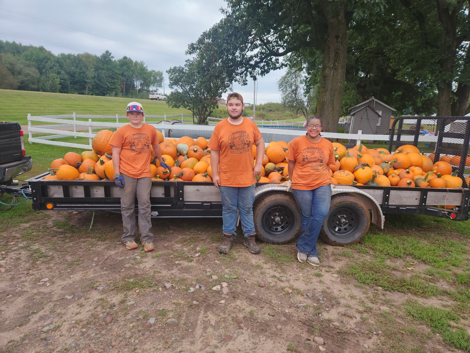 Farm crew in orange shirts beside a trailer loaded with pumpkins